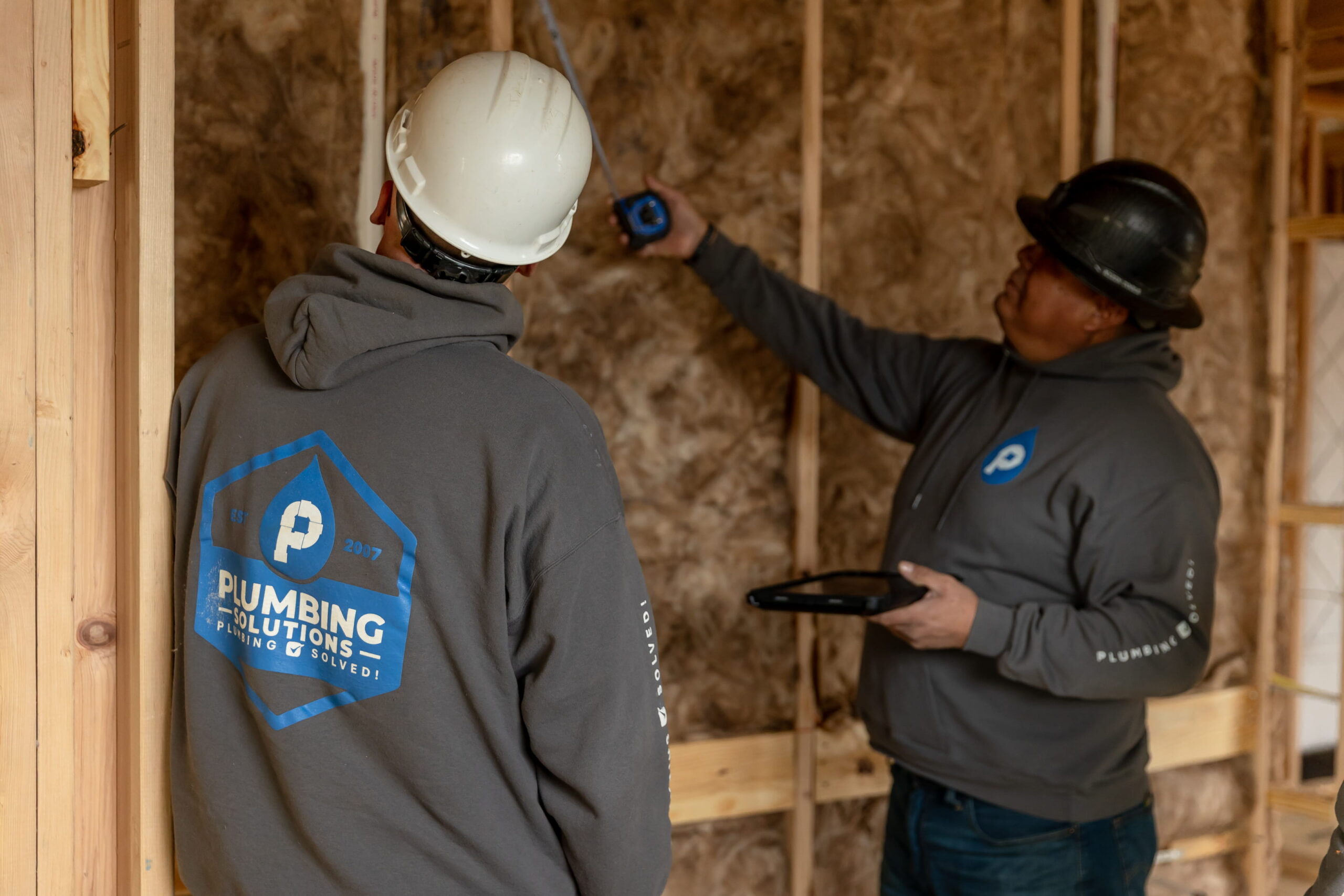 Plumbing Solutions LLC team measuring wall framing for plumbing placement