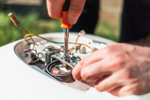 Plumbing Solutions LLC technician repairing internal components inside an electric water heater unit.