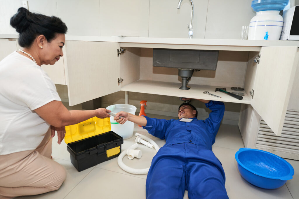 Plumbing Solutions LLC technician repairing under-sink plumbing during residential clogged drain repair service.