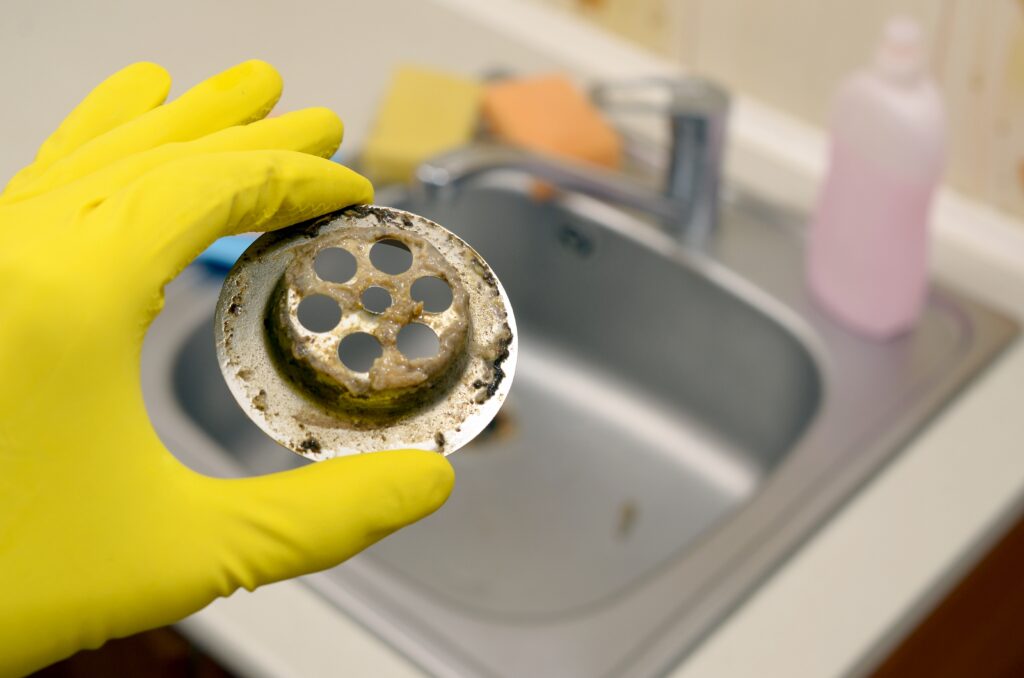 Plumbing Solutions LLC technician holding a clogged sink drain cover showing grease buildup and debris removed during professional drain cleaning.