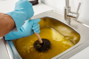 Plumbing Solutions LLC plumber plunging a clogged kitchen sink filled with standing water during residential drain repair service.