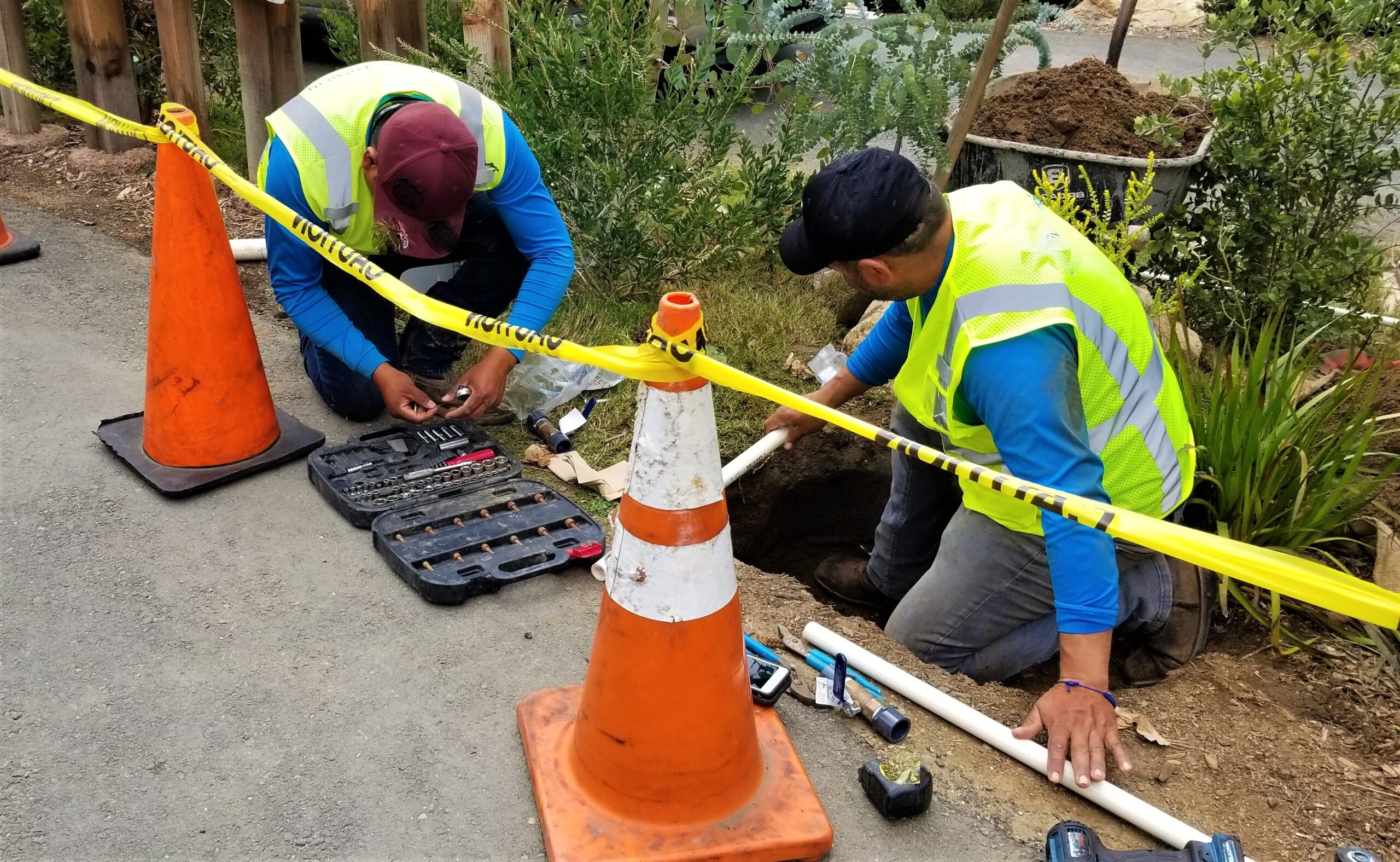 Plumbing Solutions LLC crew excavating a residential yard to access a damaged underground sewer line with safety cones and caution tape.