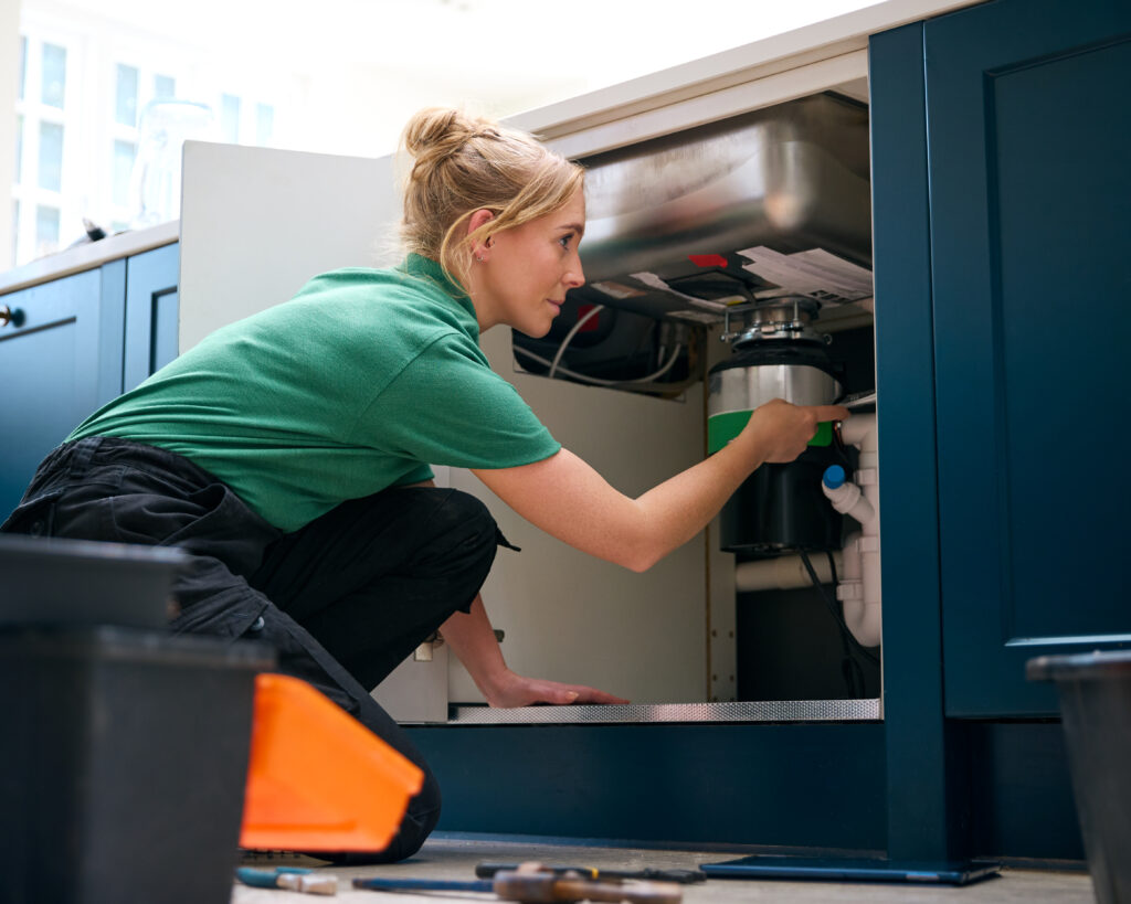 Plumbing Solutions LLC technician inspecting and adjusting a garbage disposal unit beneath a kitchen sink.