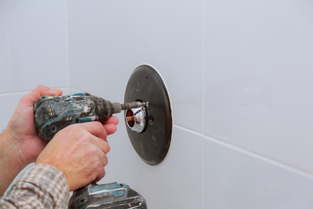 Plumbing Solutions LLC technician installing a new shower mixer valve behind a bathroom wall plate during replacement.