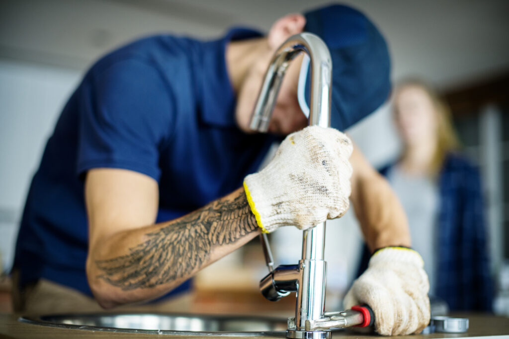 Plumbing Solutions LLC plumber tightening a kitchen faucet with a wrench at the sink