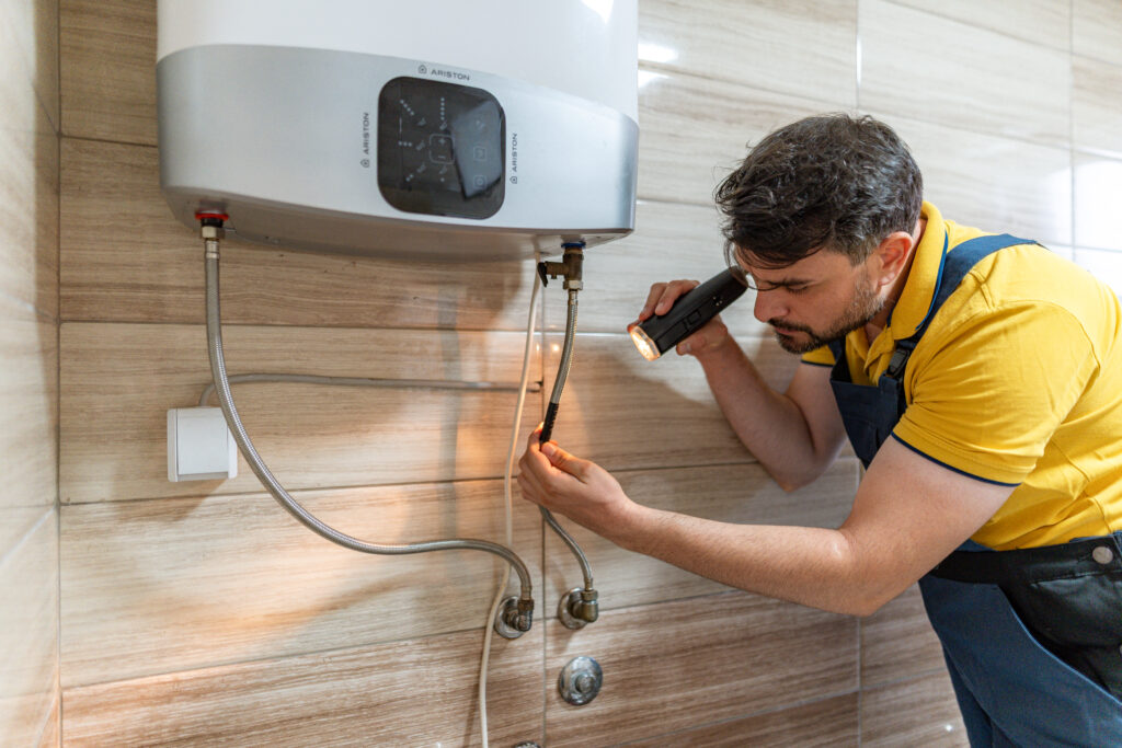 Plumbing Solutions LLC technician inspecting water heater connections with a flashlight during a maintenance check.