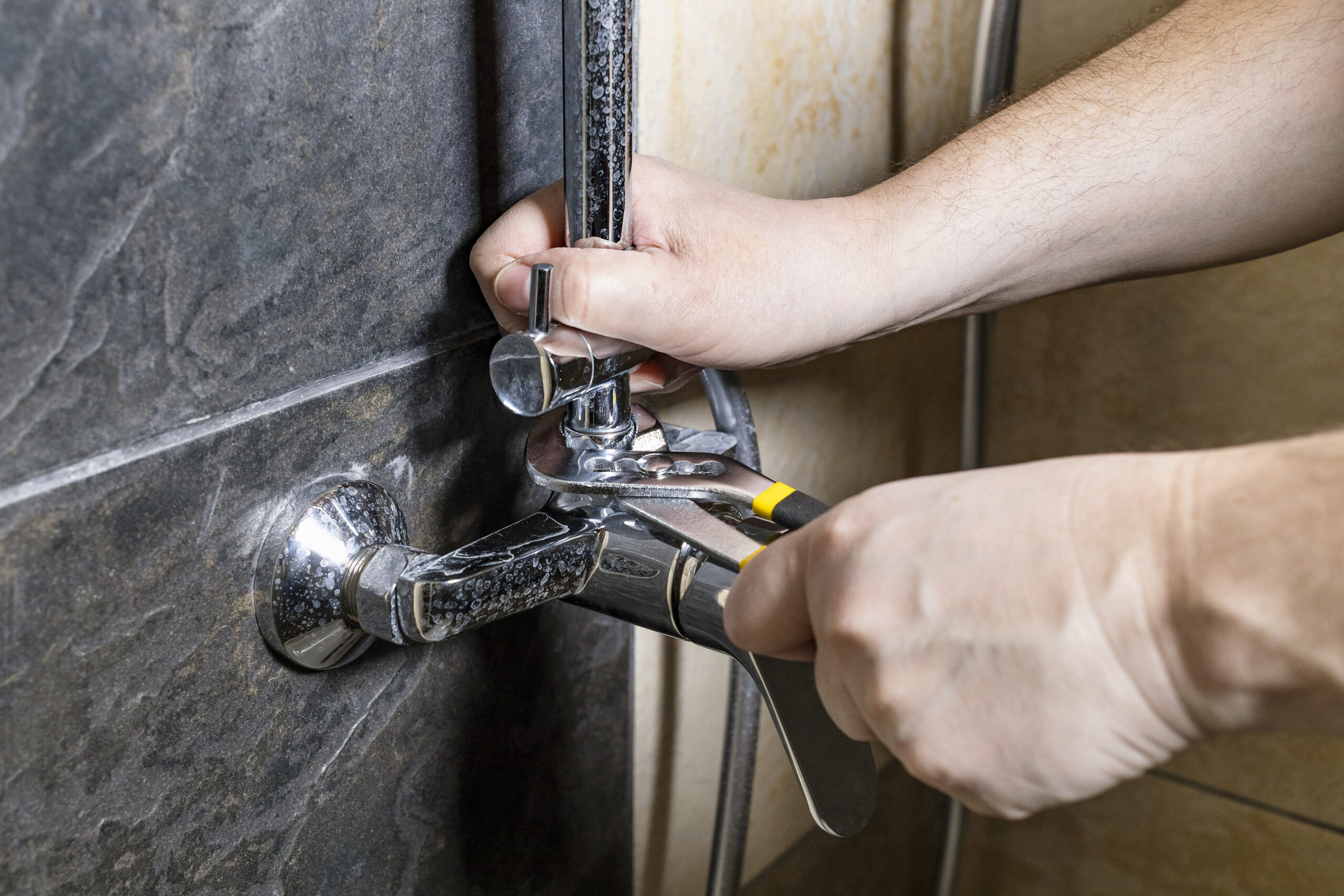 Plumbing Solutions LLC technician replacing a shower valve on a tiled bathroom wall to fix pressure and temperature issues.