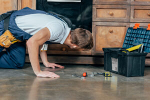 Plumber inspecting plumbing access beneath a kitchen slab with tools and toolbox during slab leak evaluation.