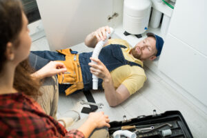Plumbing Solutions LLC technician reviewing under-sink drain components with a homeowner during a kitchen repair.