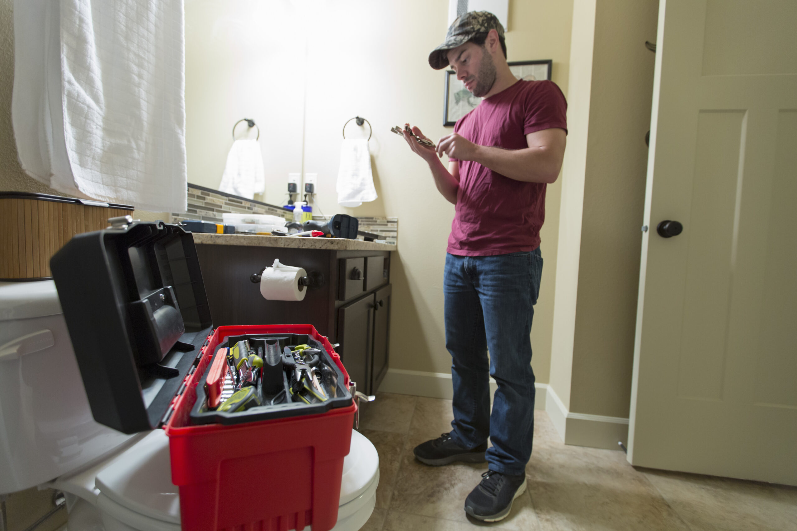 Plumbing Solutions LLC technician inspecting bathroom plumbing near a toilet during residential repair service.