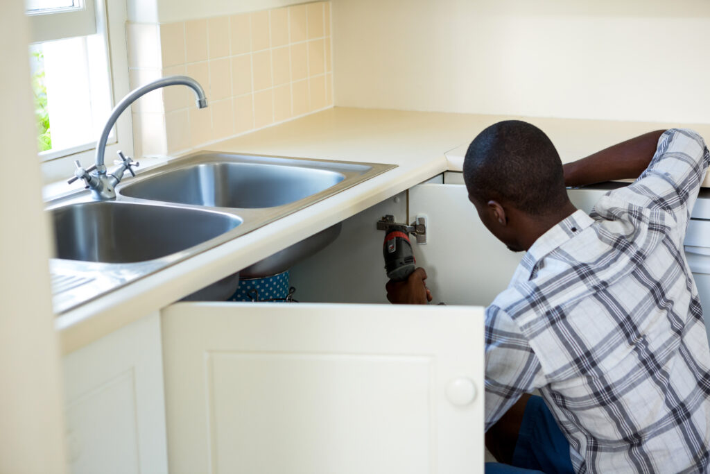 Plumbing Solutions LLC technician repairing under-sink kitchen plumbing inside a residential cabinet.