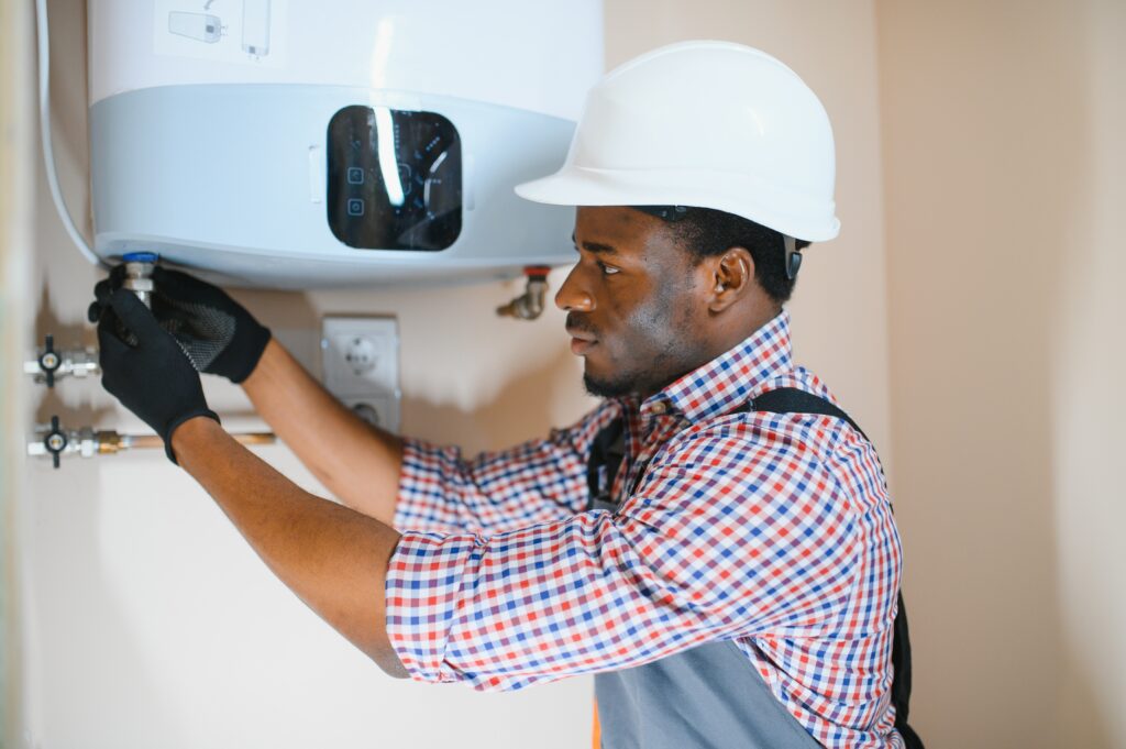 Technician adjusting plumbing connections on a wall-mounted tankless water heater during installation.