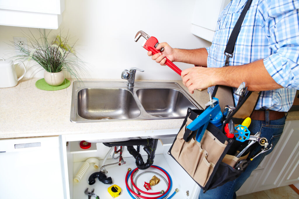 Plumbing Solutions LLC technician using a plunger to clear a clogged bathroom sink with plumbing tools arranged on the floor nearby.