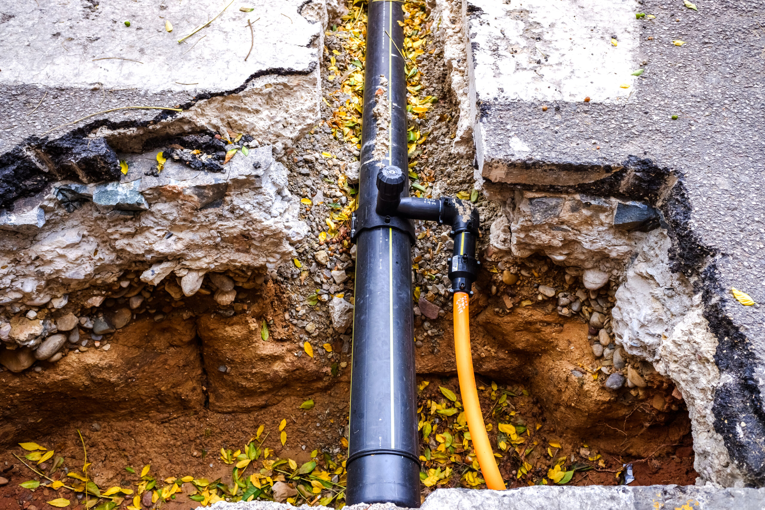 Sewer line repair in progress with a replacement pipe section installed in an open trench beside a paved surface by Plumbing Solutions LLC.
