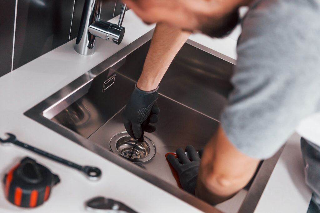 Plumbing Solutions LLC technician repairing a clogged kitchen sink drain inside a residential home kitchen.