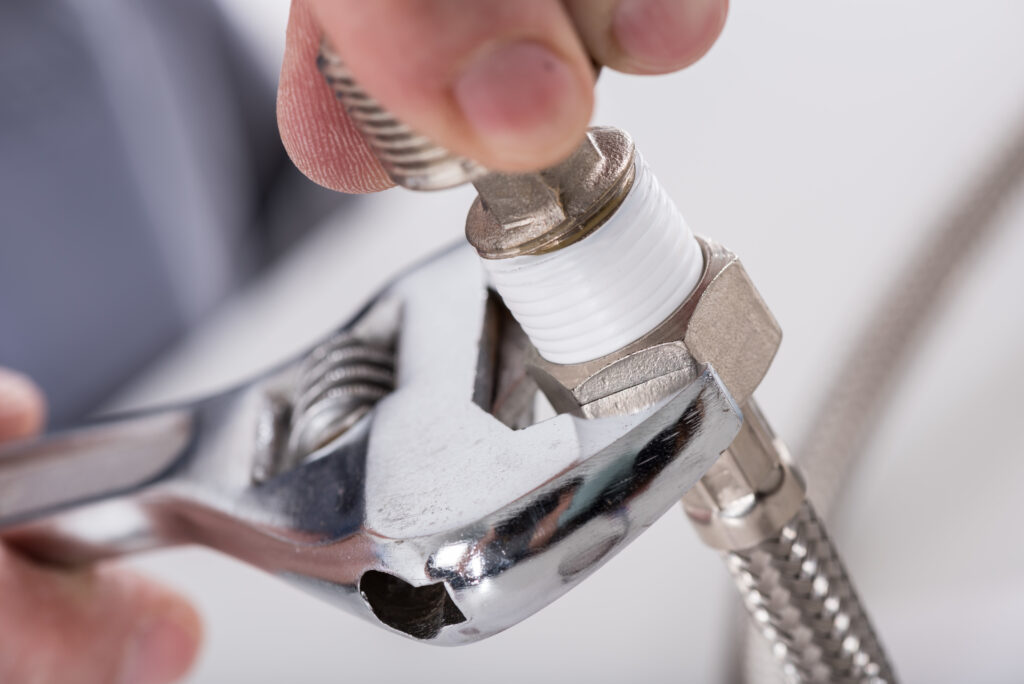 A Plumbing Solutions LLC technician tightens a bathroom water supply hose with a wrench while performing a plumbing installation or repair.