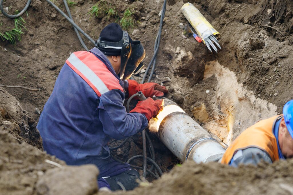 Technician welding a section of underground sewer pipe in an open trench during a sewer line repair project.