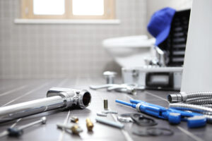 Plumbing tools and pipe fittings are arranged on a bathroom floor during a residential toilet and plumbing repair setup by Plumbing Solutions LLC.