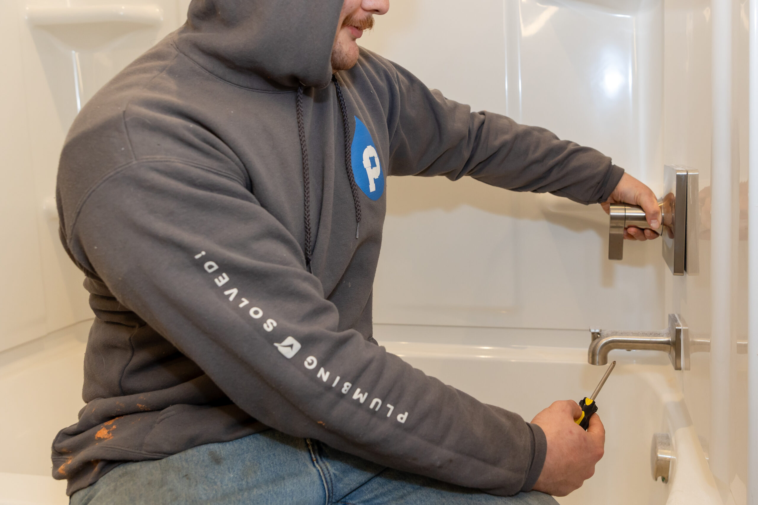 Plumbing Solutions LLC technician repairs a bathtub faucet and shower handle inside a residential bathroom.