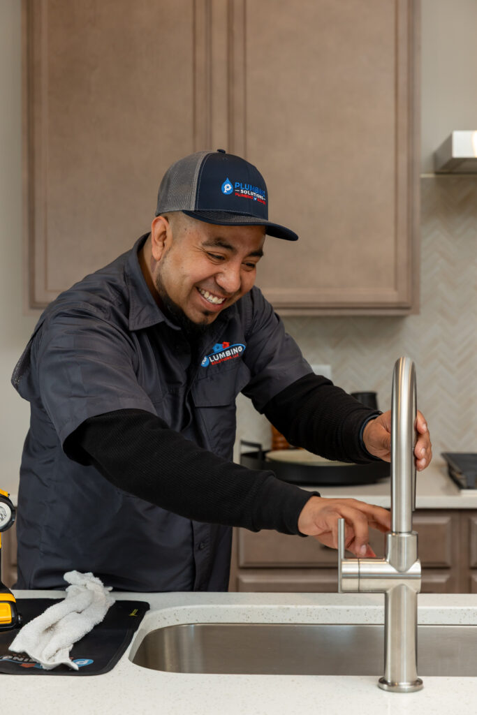 Licensed plumber adjusting and testing a kitchen faucet during a leak diagnosis and repair service.