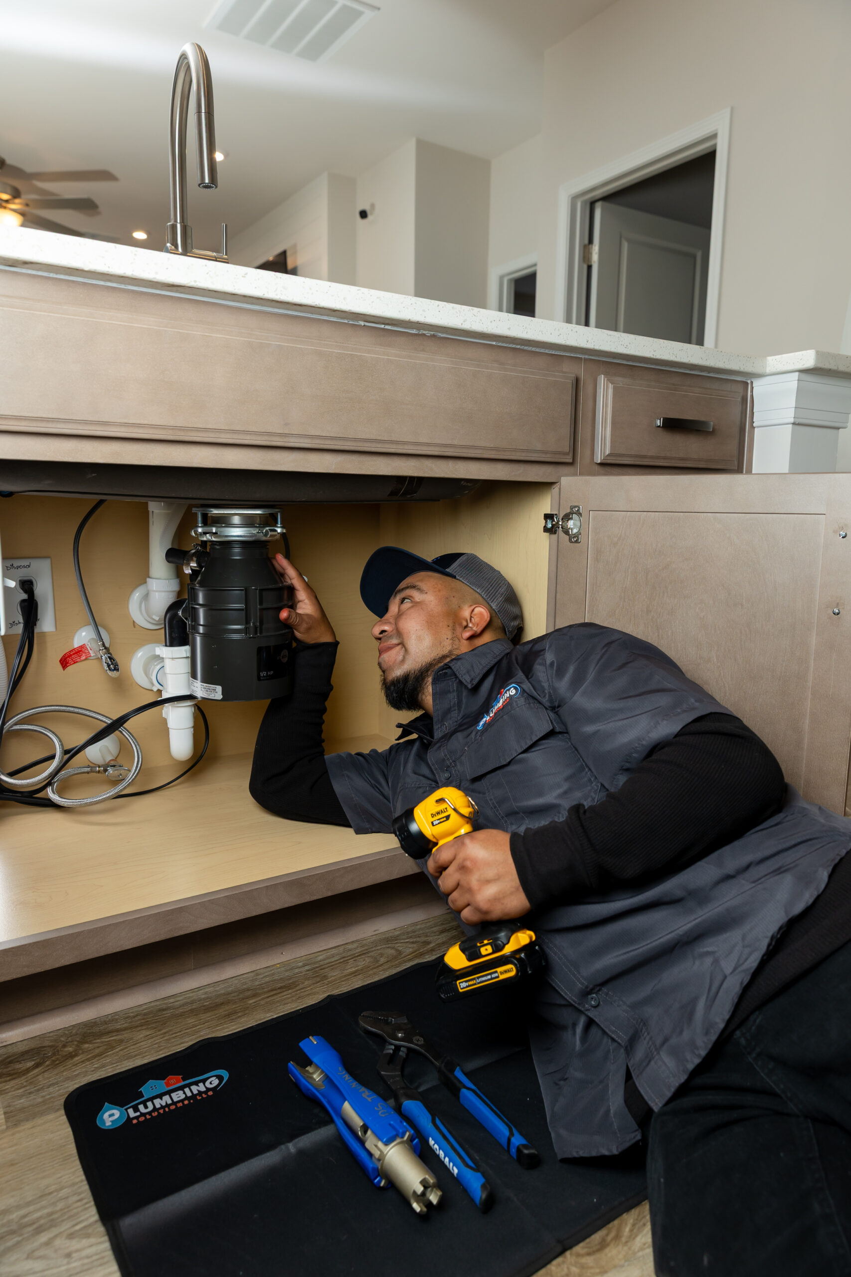 Plumbing Solutions LLC plumber installing a garbage disposal beneath a kitchen sink during a plumbing service.