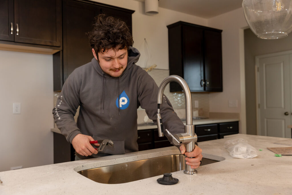 Plumbing technician installing a new kitchen faucet as part of a repair or fixture replacement project.