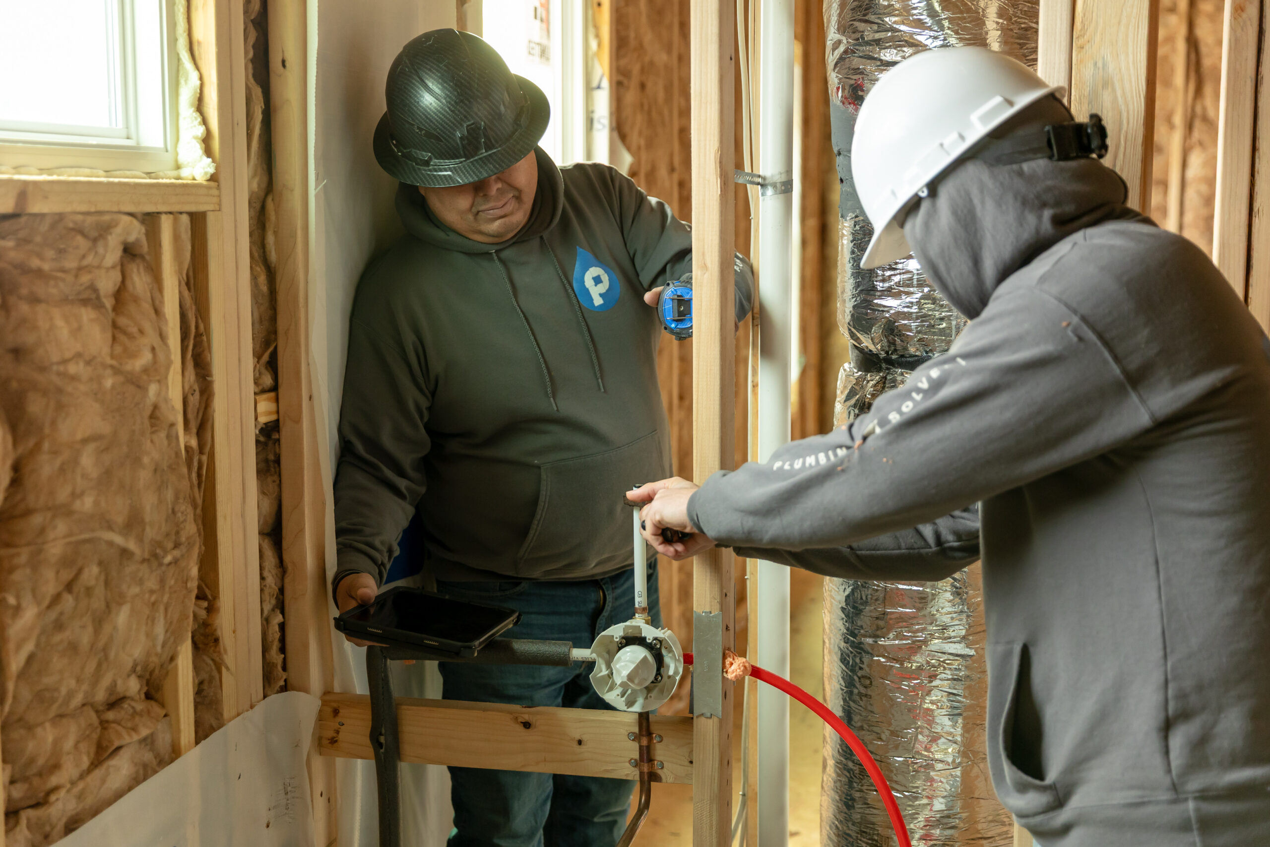 Plumbing Solutions LLC plumbers measuring water supply pipe placement inside residential wall framing during a plumbing installation project.