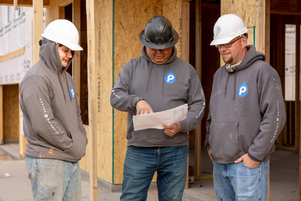 Plumbing Solutions LLC team reviewing construction plans and plumbing layouts at an active job site.