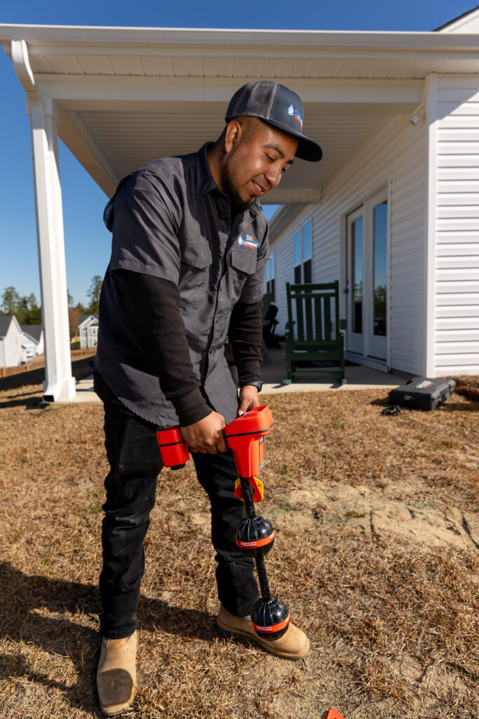 Plumbing Solutions LLC technician operating a drain auger outside a residential property to diagnose and clear sewer line blockages.