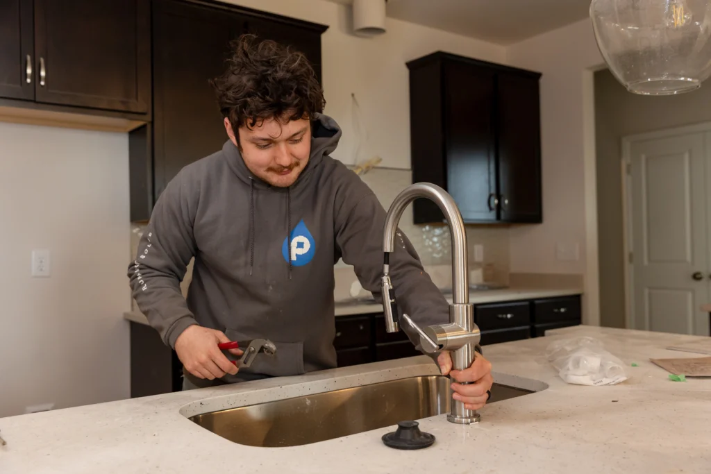 Professional plumber repairing a kitchen sink faucet and checking fixture connections for leaks.